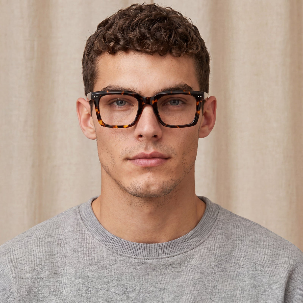 A man wearing tortoiseshell eyeglasses with thick black frames and a gray crewneck sweatshirt