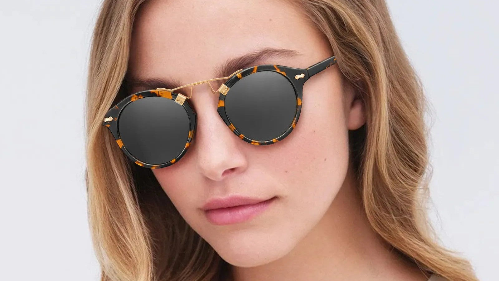 Woman wearing round tortoiseshell sunglasses with dark lenses