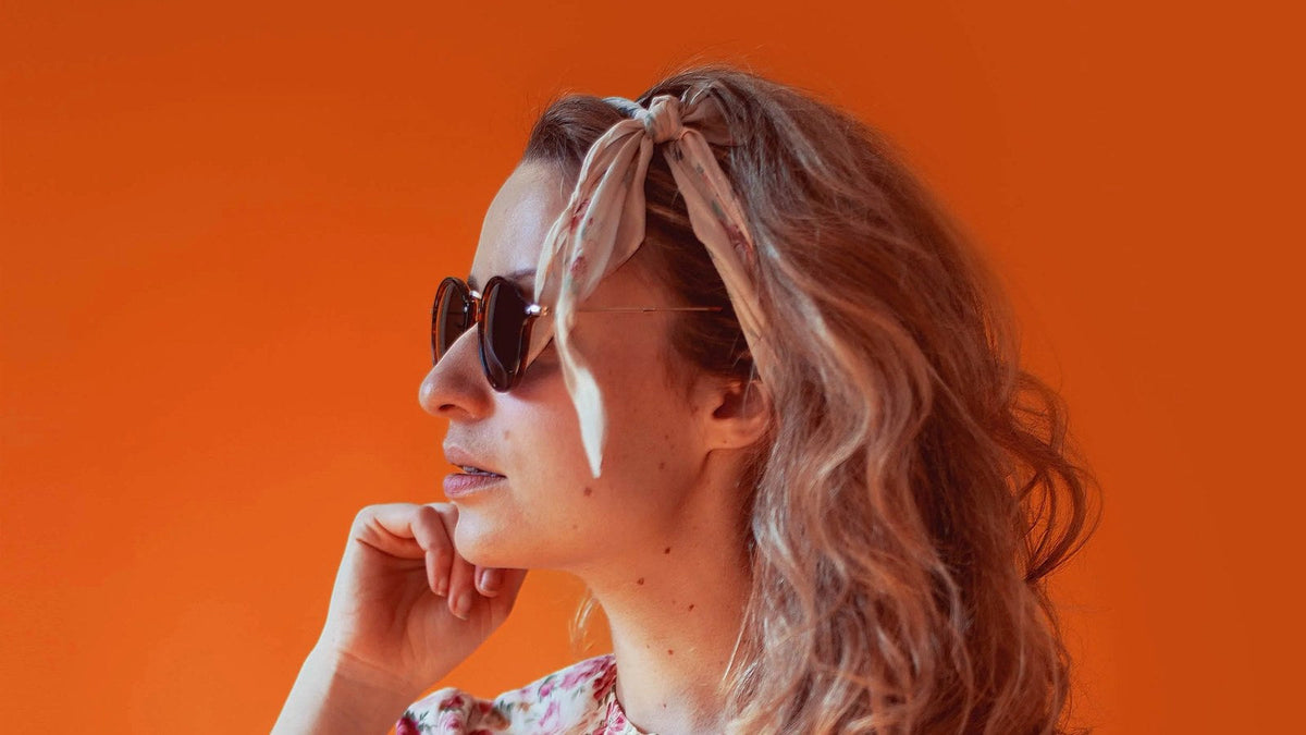 Woman wearing lightweight round sunglasses against an orange background