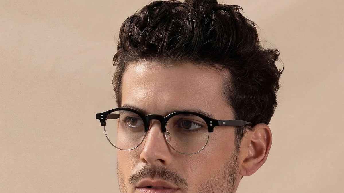 Man wearing black round semi-rimless eyeglasses against a warm beige background