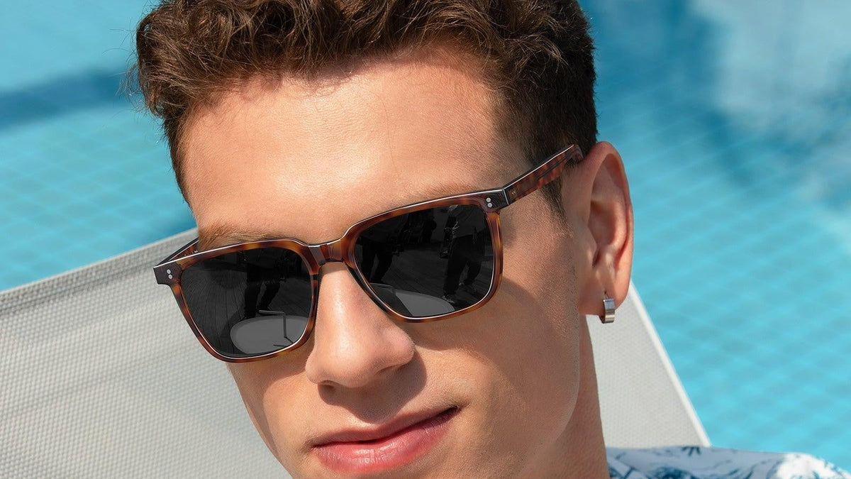 Man wearing tortoiseshell retro square sunglasses by a pool