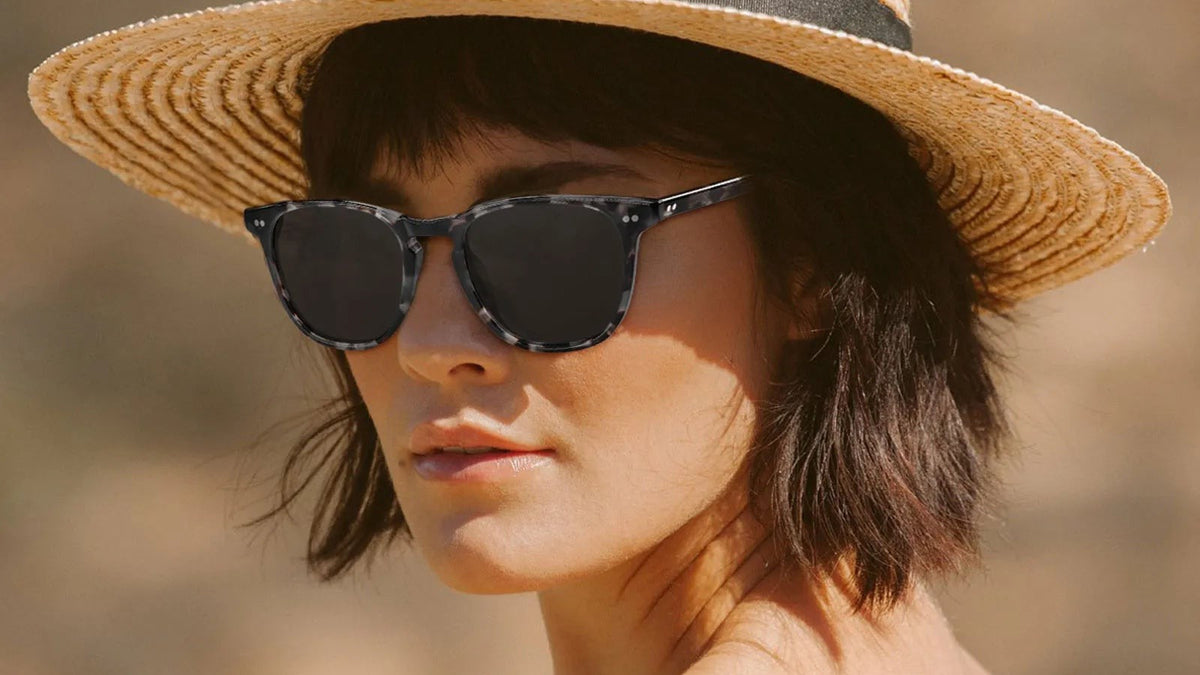 Woman wearing dark tortoiseshell angular sunglasses and a straw hat