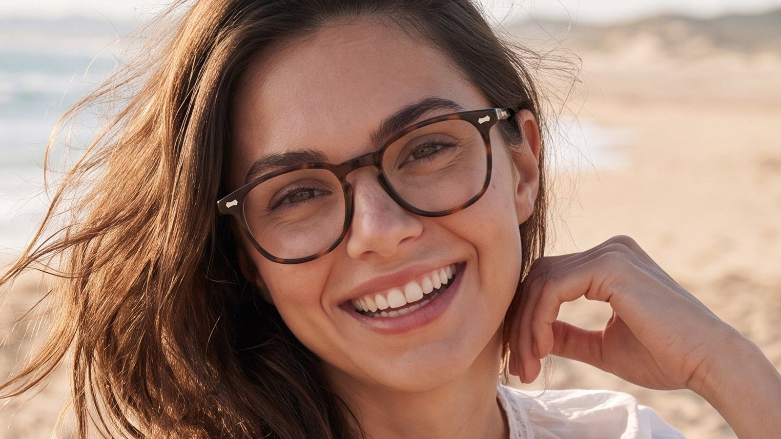 Smiling woman on a beach wearing round tortoiseshell eyeglasses
