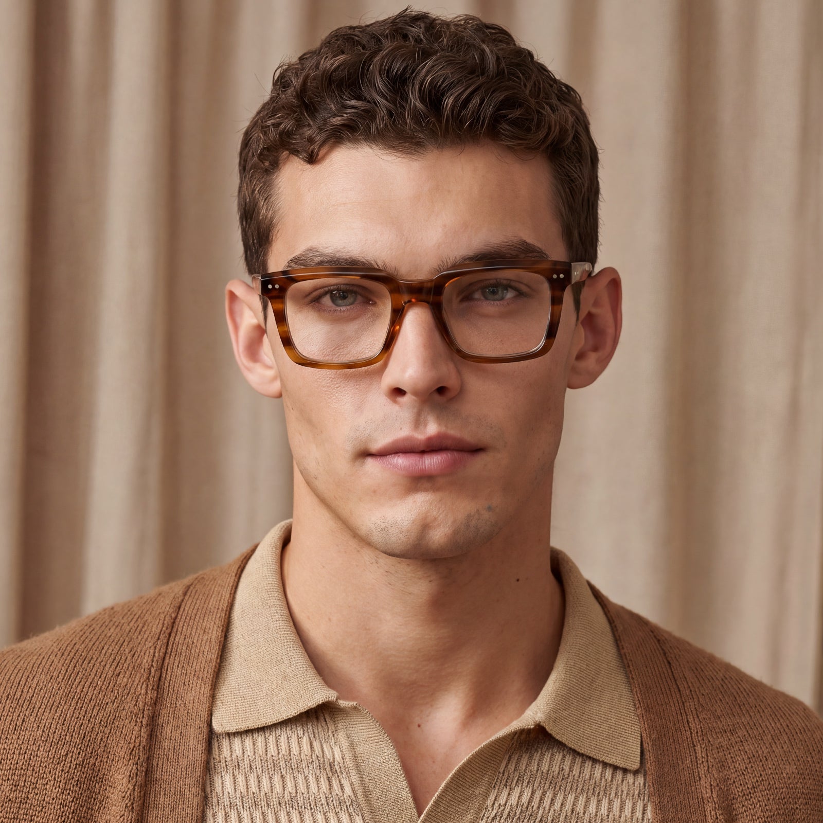 A close-up portrait of a man wearing thick, square tortoiseshell acetate eyeglasses with a warm brown and amber tone men brown eyeglasses